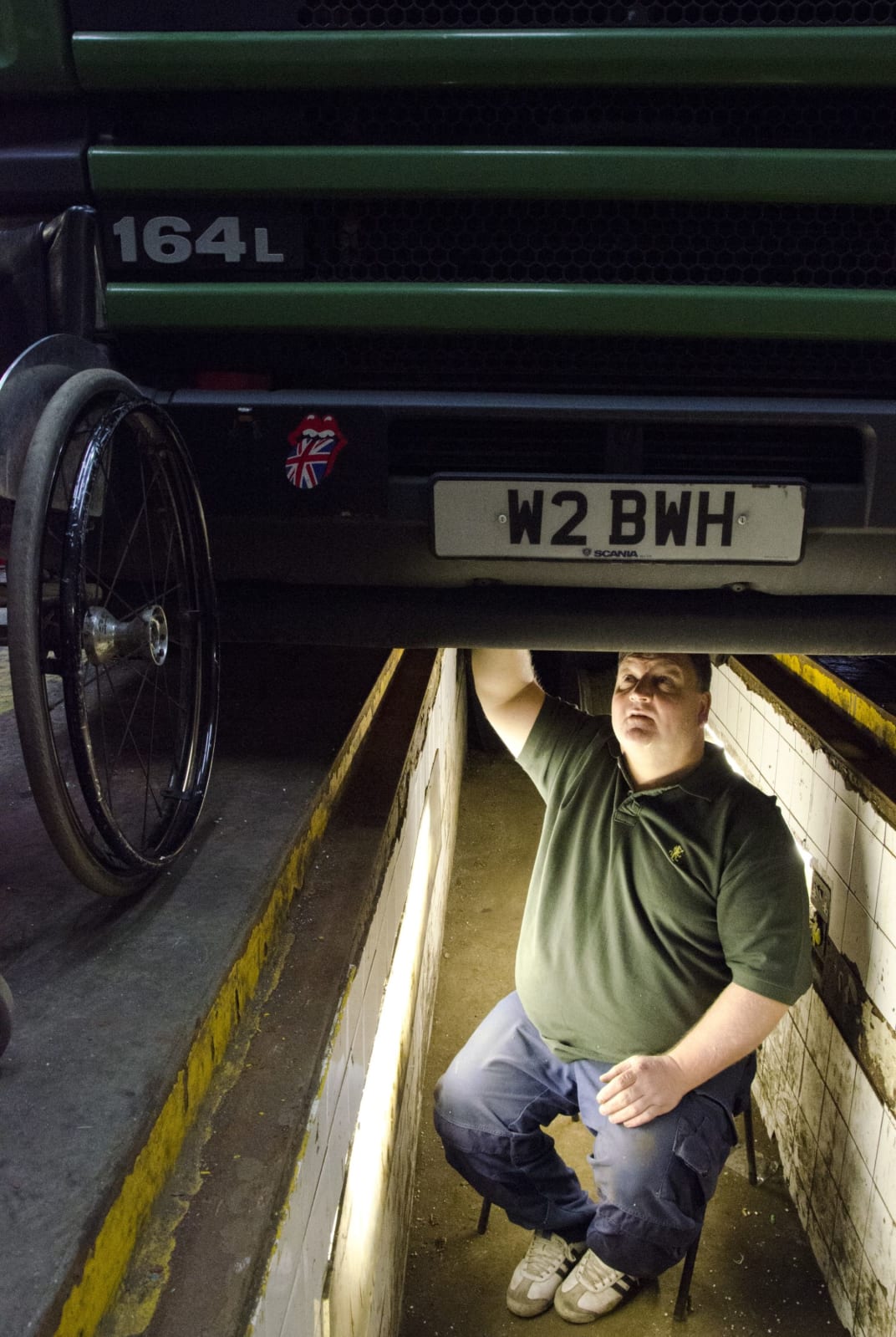 Brian working underneath a truck, with wheelchair on the side