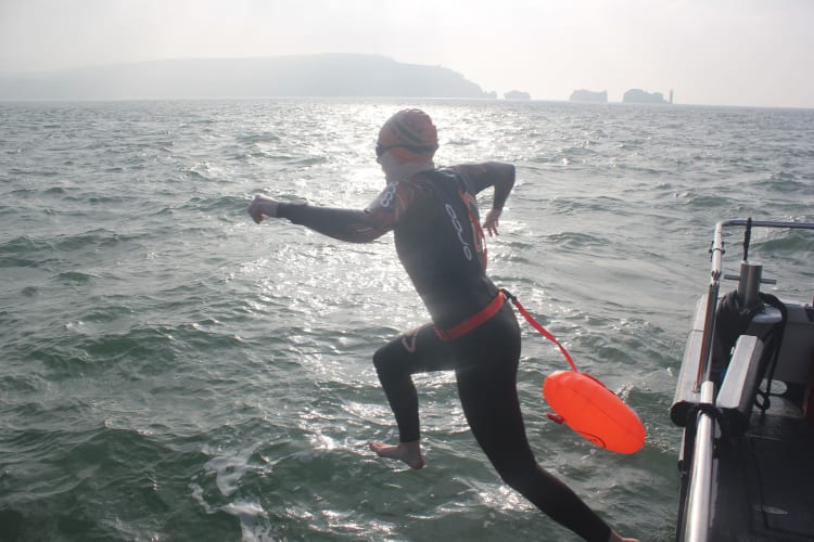 Swimmer jumping off the boat with the Needles in the distance