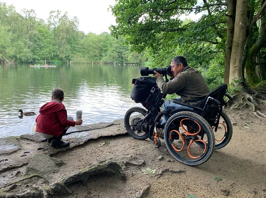 Peter in his wheelchair by a lake with his camera