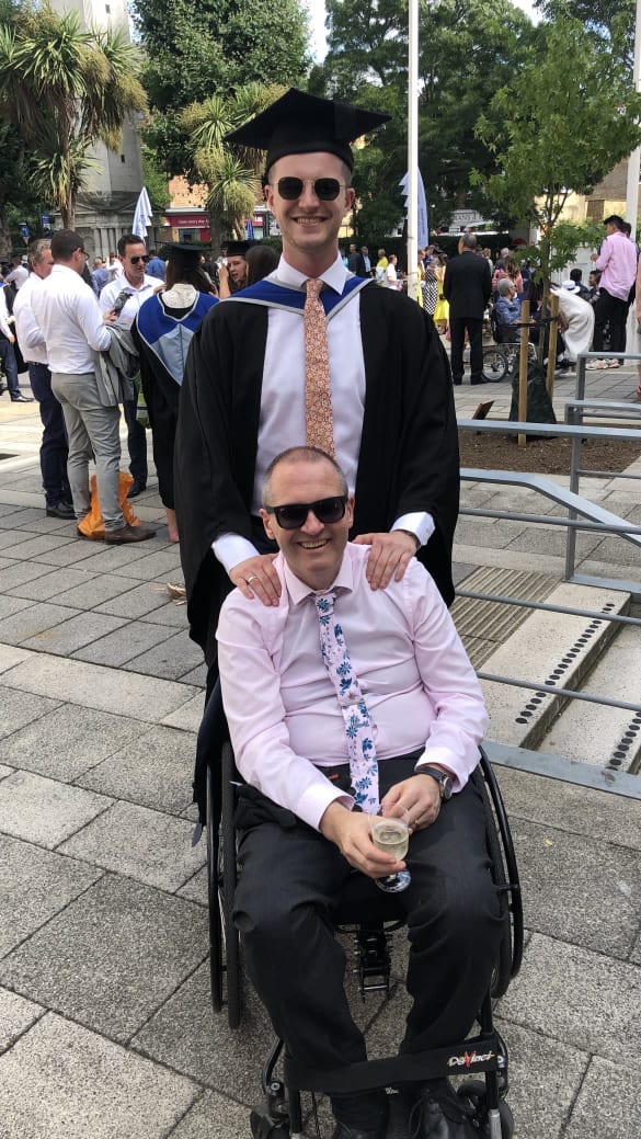 Charlie standing behind his dad sitting in a wheelchair