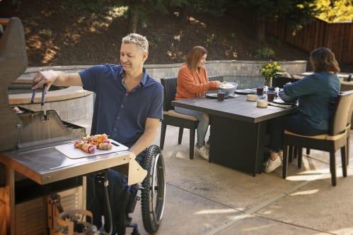 Man barbecuing with woman behind him sitting at a table