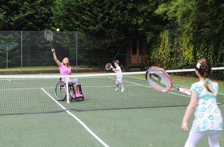 Lady in wheelchair playing tennis with her children